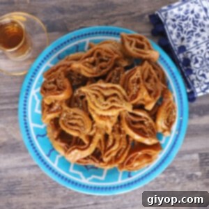 A blue plate full of chebakia cookies sprinkled with sesame seeds with cups of Moroccan tea on the side.