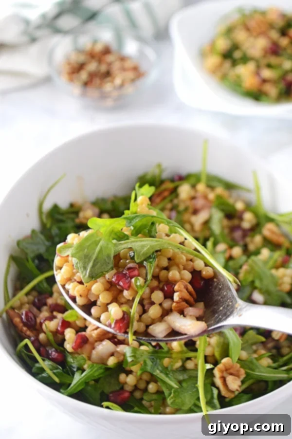 A spoon scooping some of the Mediterranean couscous salad with the whole bowl in the back.