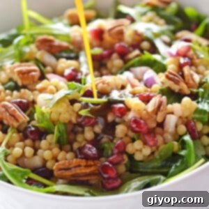 Pearl couscous salad in a deep white bowl with vinegrette pouring over it.