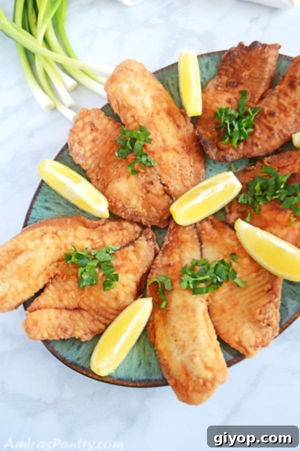 Crispy fried tilapia fillets garnished with fresh lemon wedges on an oval green serving platter, ready to be enjoyed.