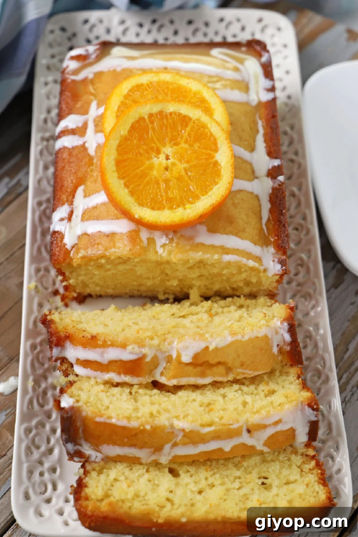 A beautifully glazed orange loaf cake on a serving platter, surrounded by fresh orange slices and ready for afternoon tea.