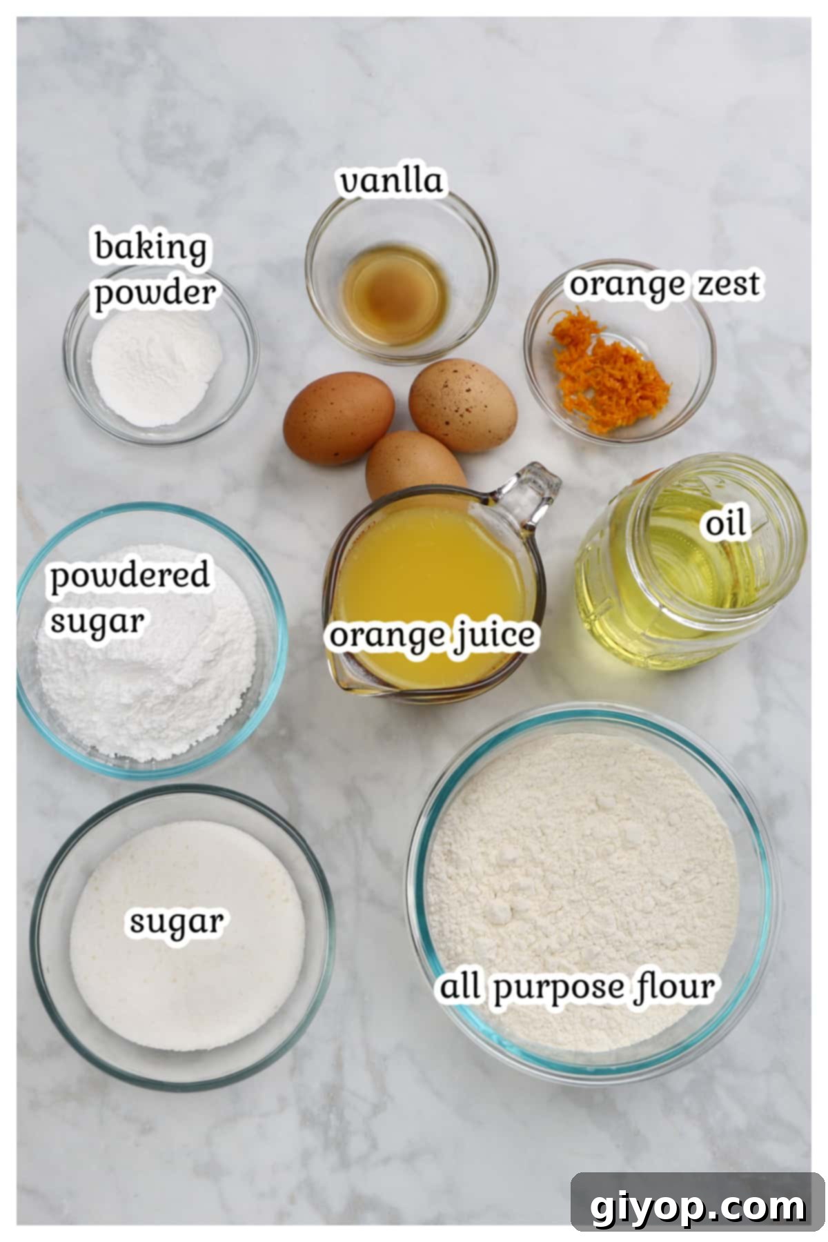A collection of ingredients for an orange cake laid out on a marble surface, including fresh oranges, flour, eggs, and oil.