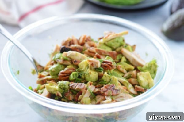 A big serving bowl filled with creamy avocado chicken salad, with a serving spoon nestled within, inviting diners to indulge.