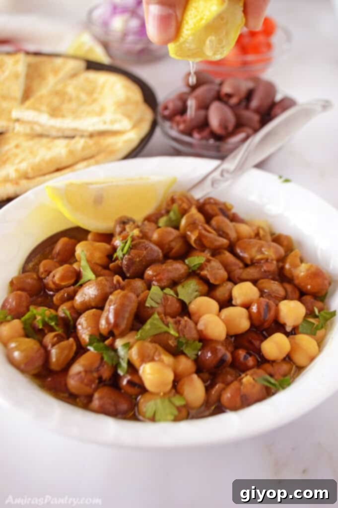 A hand squeezing fresh lemon juice over a bowl of Ful Medames, enhancing its flavor.