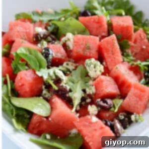 A white plate with watermelon and feta salad, with some pita bread pieces visible in the background.
