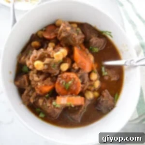 A big bowl of beef stew with a spoon in it.