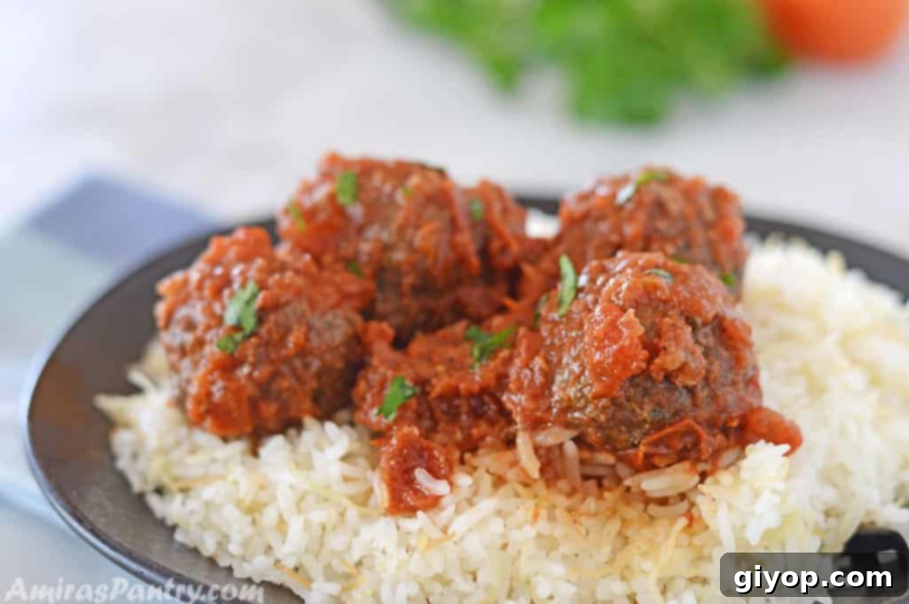 Moroccan meatballs with tomato sauce, served over a bed of fluffy rice on an elegant black plate, garnished with fresh herbs.