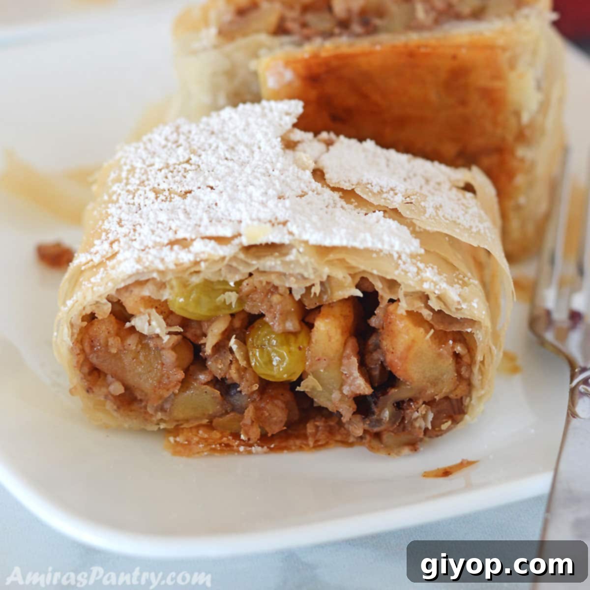 Flaky Phyllo Apple Strudel 2 A slice of golden-brown apple strudel, garnished with powdered sugar, resting on a white plate with a fork beside it.