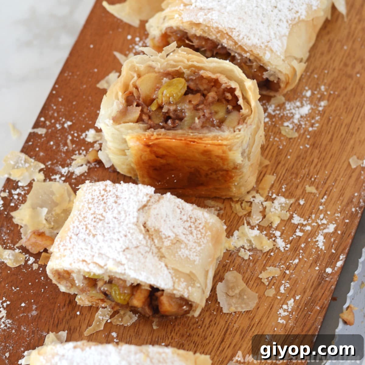 Flaky Phyllo Apple Strudel 3 Multiple pieces of golden-brown apple strudel arranged on a rustic wooden board, with one piece showcasing its delightful flaky layers.
