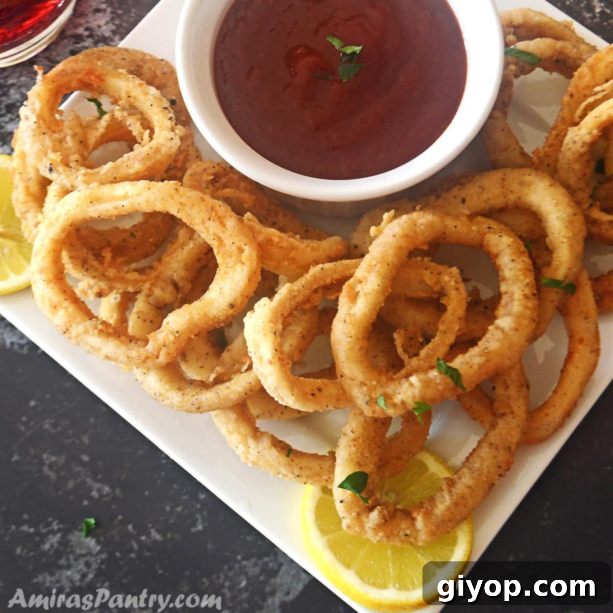 Fried calamari rings on a white serving plate with a bowl of marinara sauce in the middle.