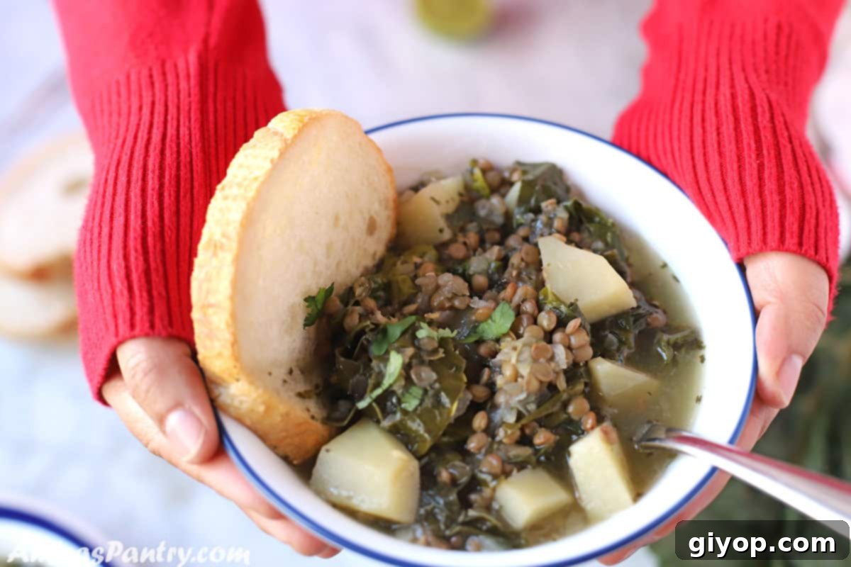 Hand holding a white bowl with Lebanese lentil soup with a piece of crusty bread.