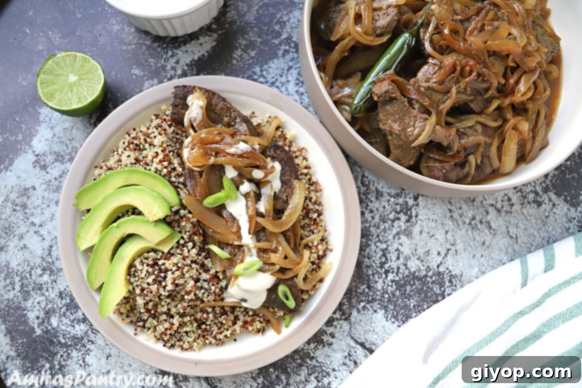 A plate featuring a serving of beef liver and onions, accompanied by quinoa and sliced avocado, resting on a concrete table next to half a lemon.