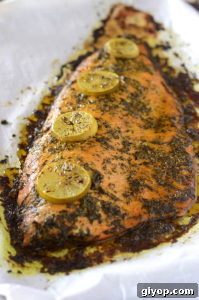 A whole salmon fillet beautifully garnished with lemon slices and fresh herbs on a baking sheet, ready to be cooked.