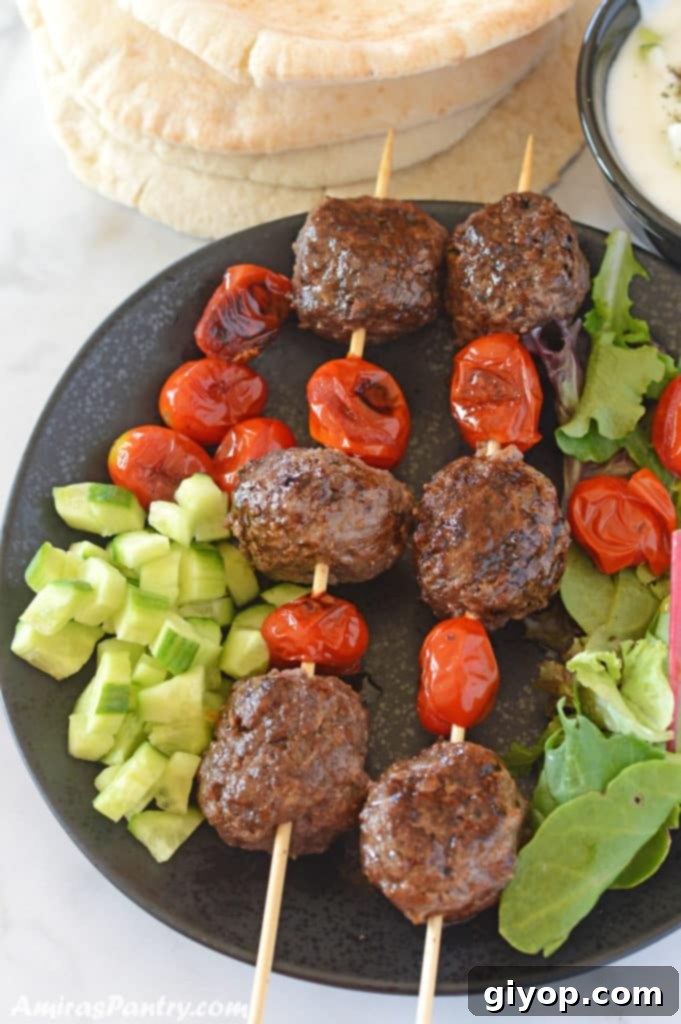 Effortless Freezer Meals 3 Kofta skewers with tomato on a black plate we diced cucumber and pita bread in the back