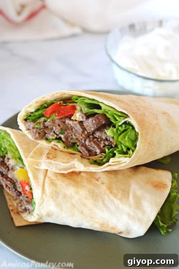 Effortless Freezer Meals 6 Beef Shawarma wrap on a dark green plate with a bowl of white shawarma sauce on the back.