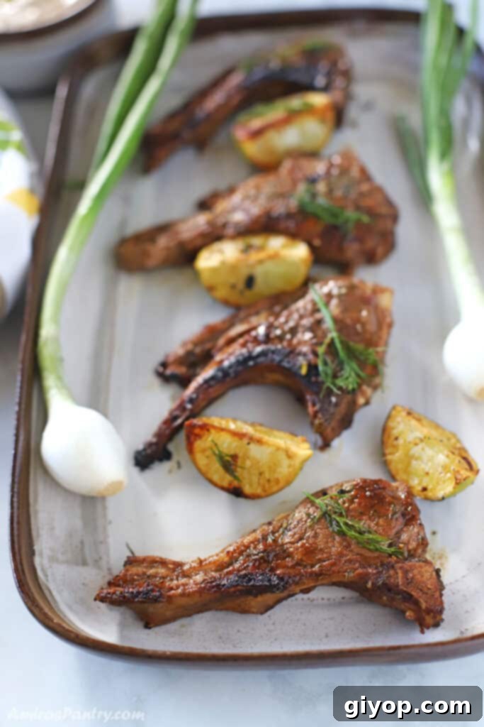 lamb chops on a serving platter with green onions and lemon wedges on the side.