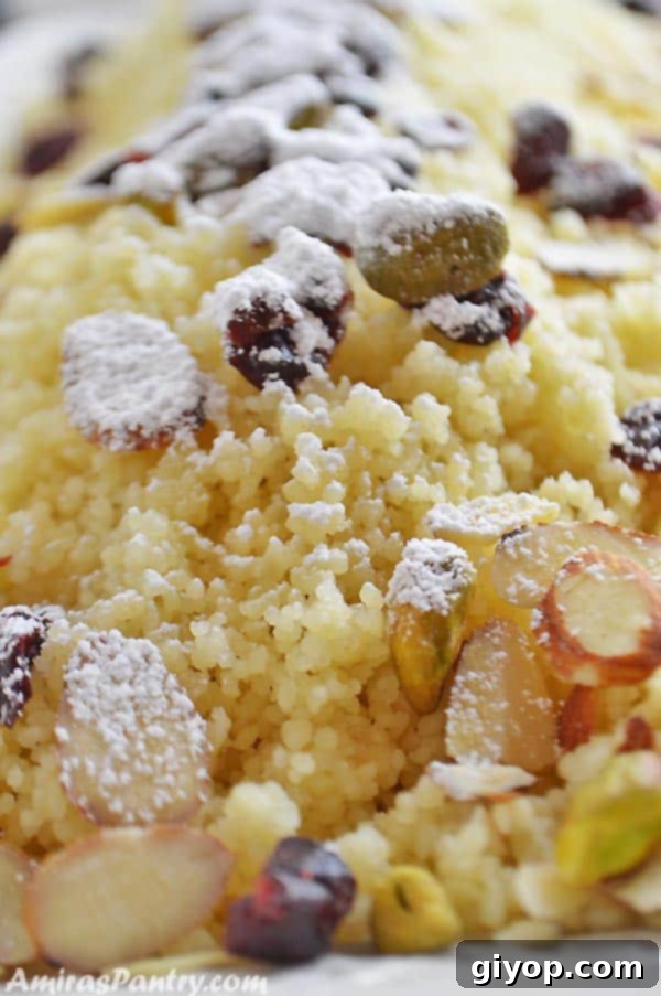 A close-up of sweet couscous garnished with pistachios, almonds, and dried cranberries, suggesting a festive and comforting dessert.
