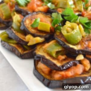 Tangy Garlic Eggplant 7 A white plate with perfectly cooked eggplant slices bathed in a rich garlic and vinegar sauce, garnished with fresh herbs.