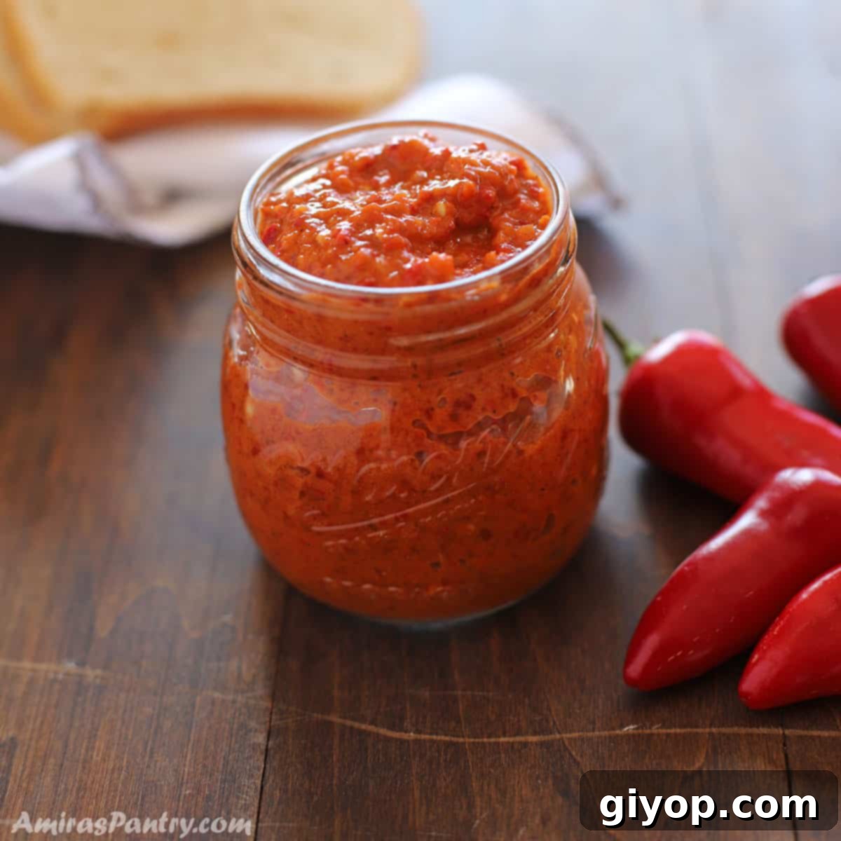 Crafting Authentic Harissa at Home 2 A jar of Harissa on a wooden surface with some chili peppers on the side and bread on the back.