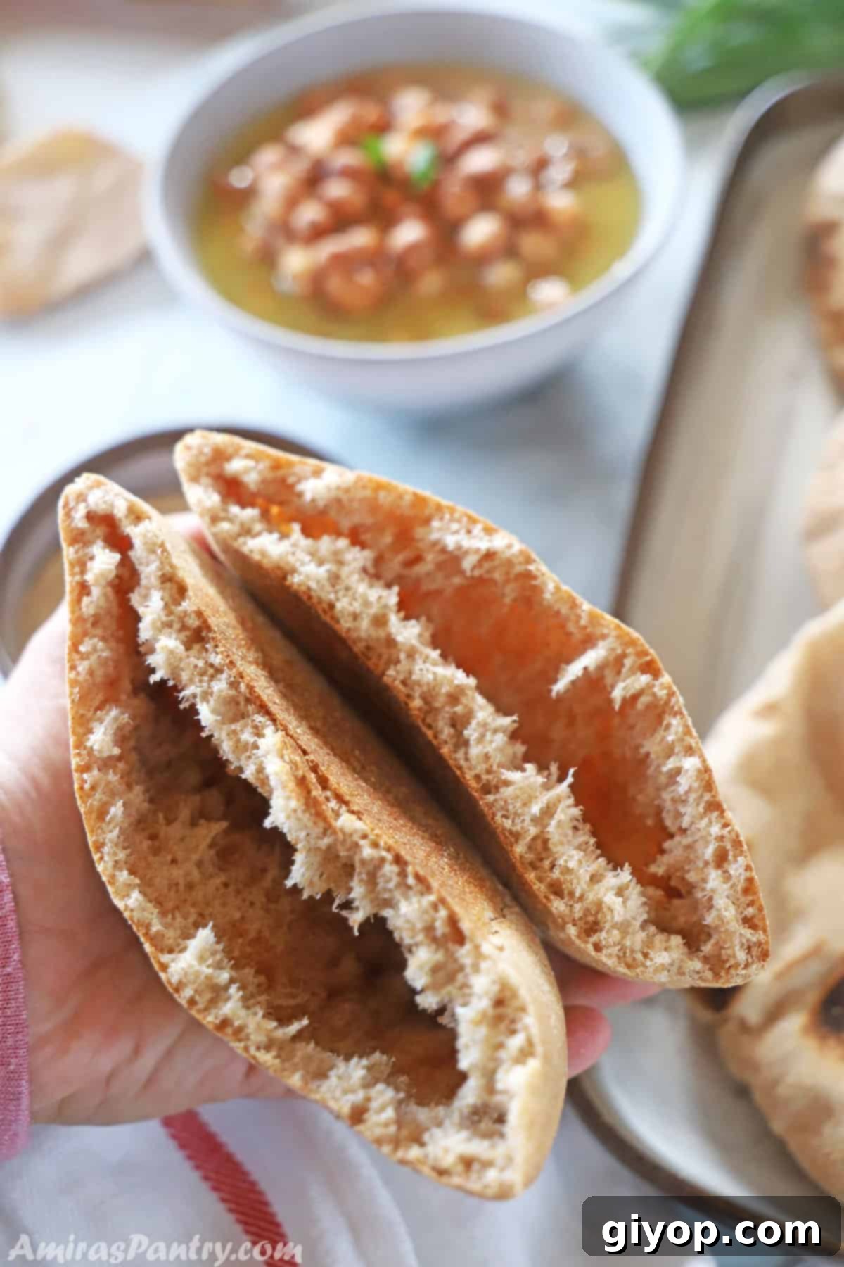 A hand holding two halves of a whole wheat pita bread, opened to reveal its hollow pocket interior.