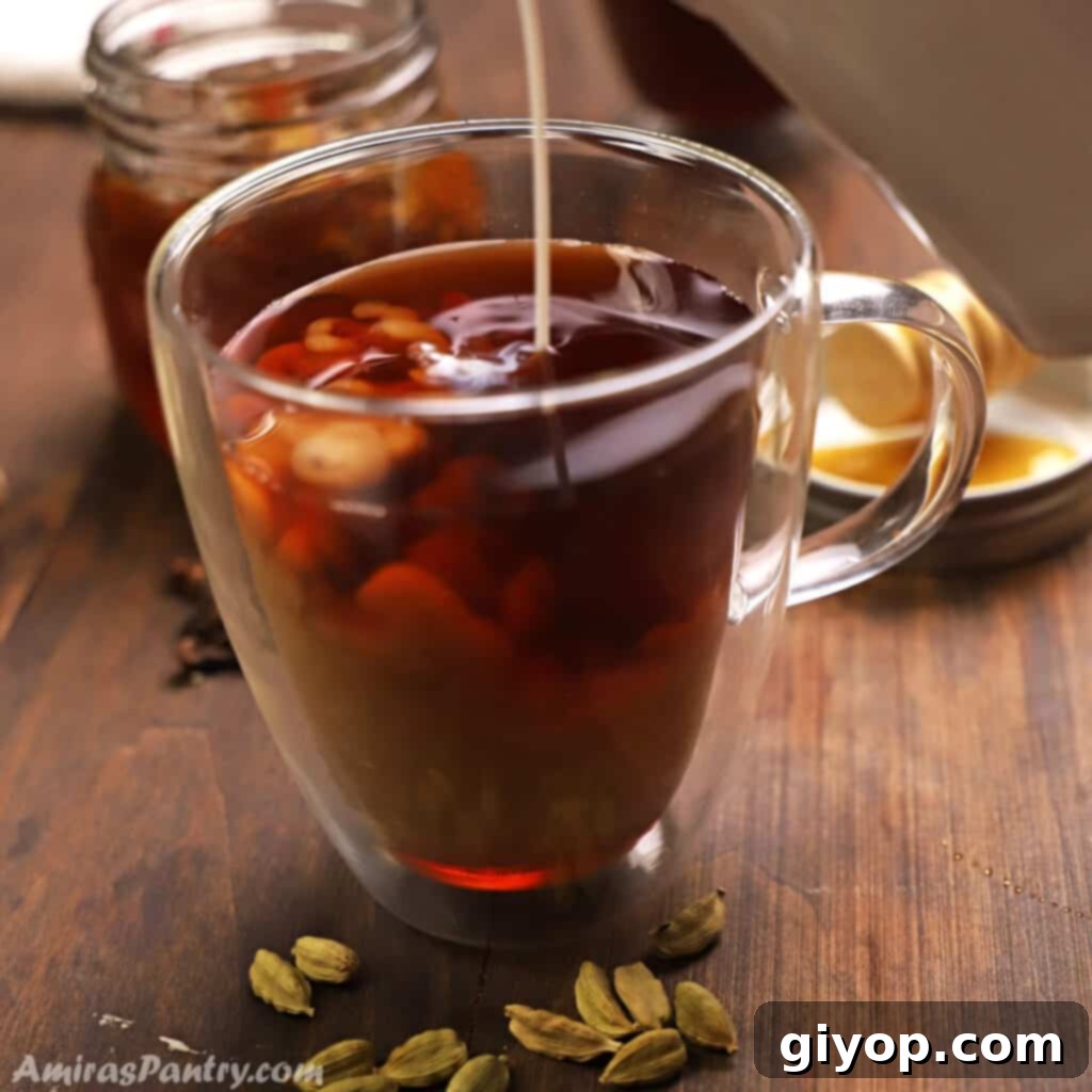 Pouring milk in a cup of cardamom tea placed on a wooden surface. The cup is steaming gently.
