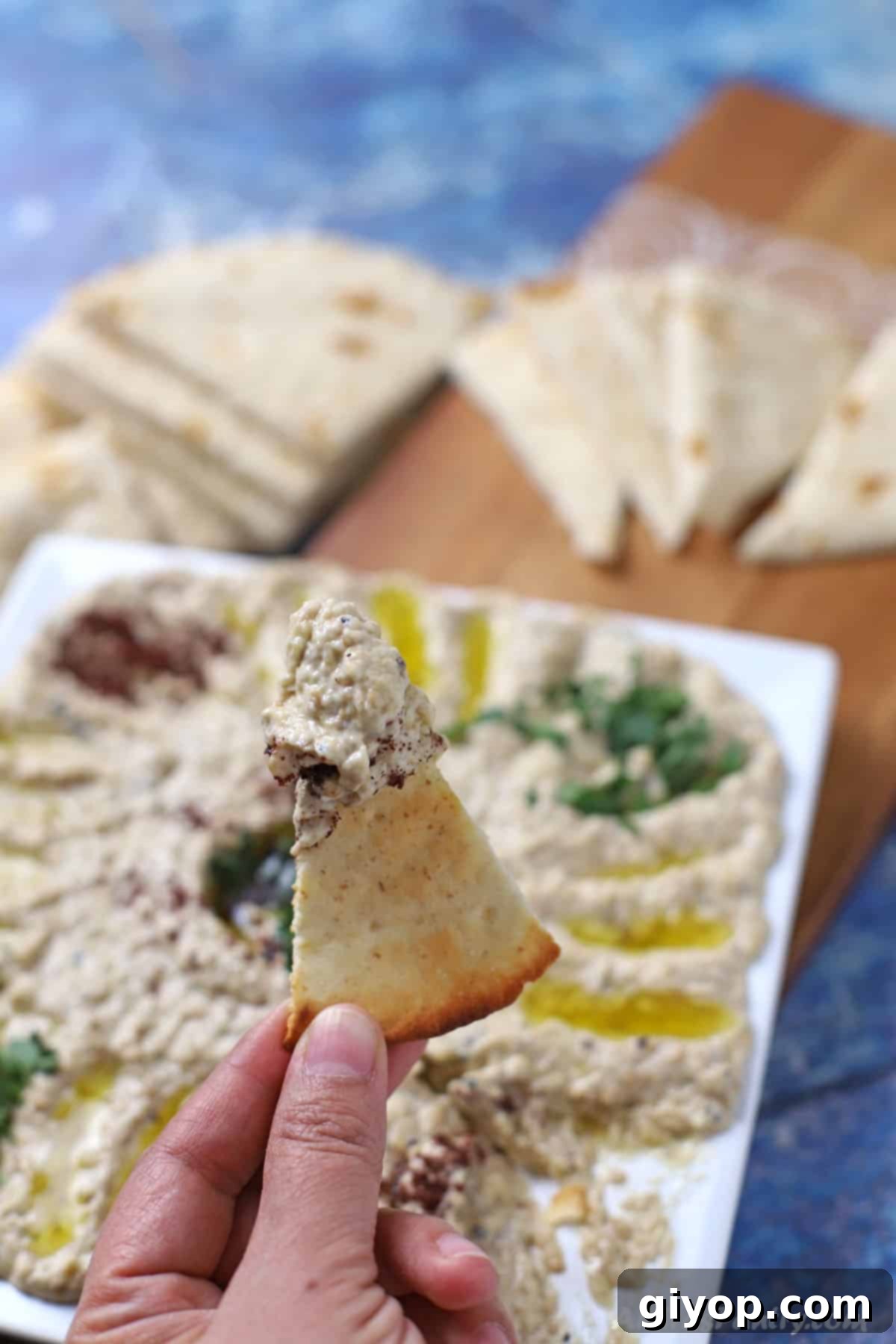 A hand holding a piece of pita wedge dipped in mutabbal.