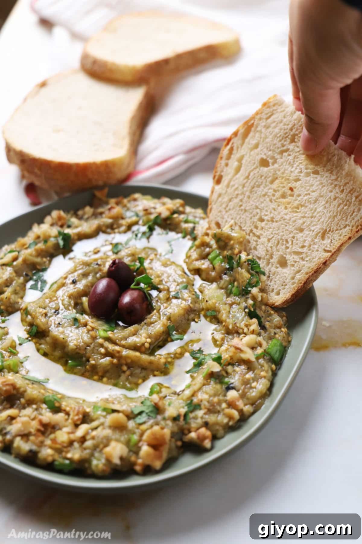 A hand dipping a piece of bread in a plate of Melitzanosalata.