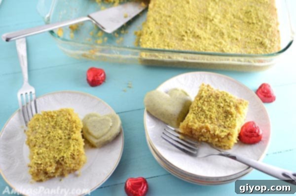 A beautifully arranged plate featuring a piece of pistachio semolina cake alongside chocolate hearts and green decor, evoking a festive or romantic theme.
