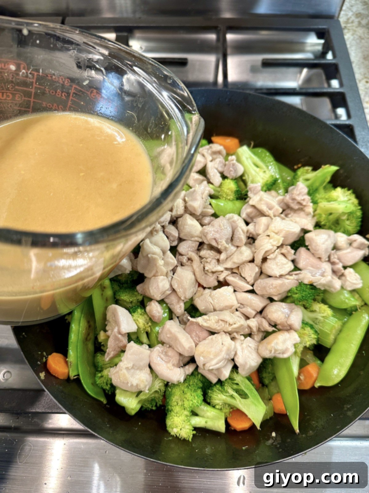 A cup of sauce for cashew chicken stir fry over a pan of veggies and chicken.