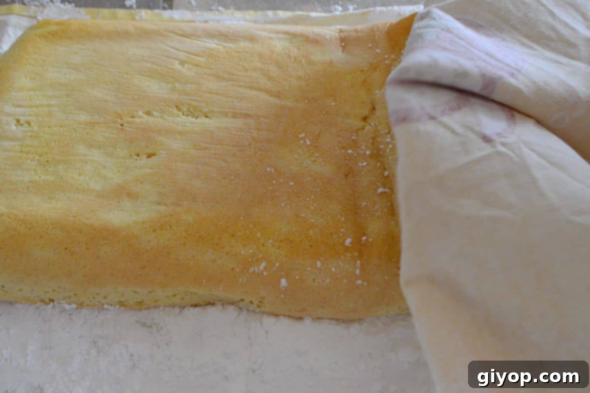 Ultimate Cinnamon Cake Roll Recipe 4 An image showing the crucial step of carefully rolling a warm Swiss roll cake with a clean towel to set its shape.