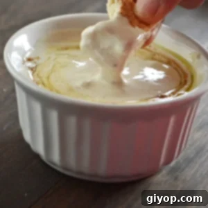 A hand dipping a piece of bread in a bowl of tahini sauce.