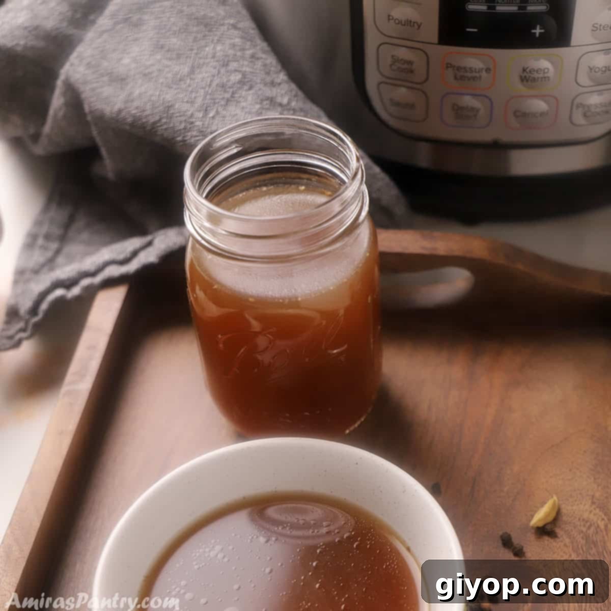 A mason jar filled with bone broth and a bowl with bone broth placed in front of an instant pot on a wooden tray.