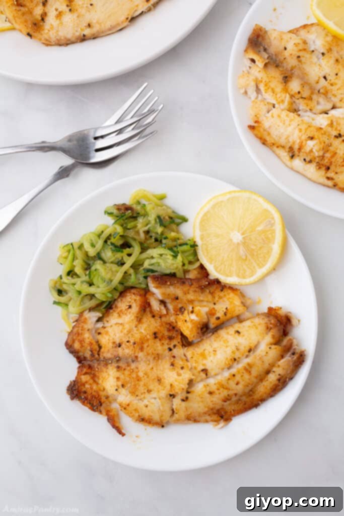 Meal Plan 4 A perfectly cooked tilapia fillet, golden and flaky, resting on a white plate alongside vibrant green vegetables and cutlery, captured from a bird's eye view.