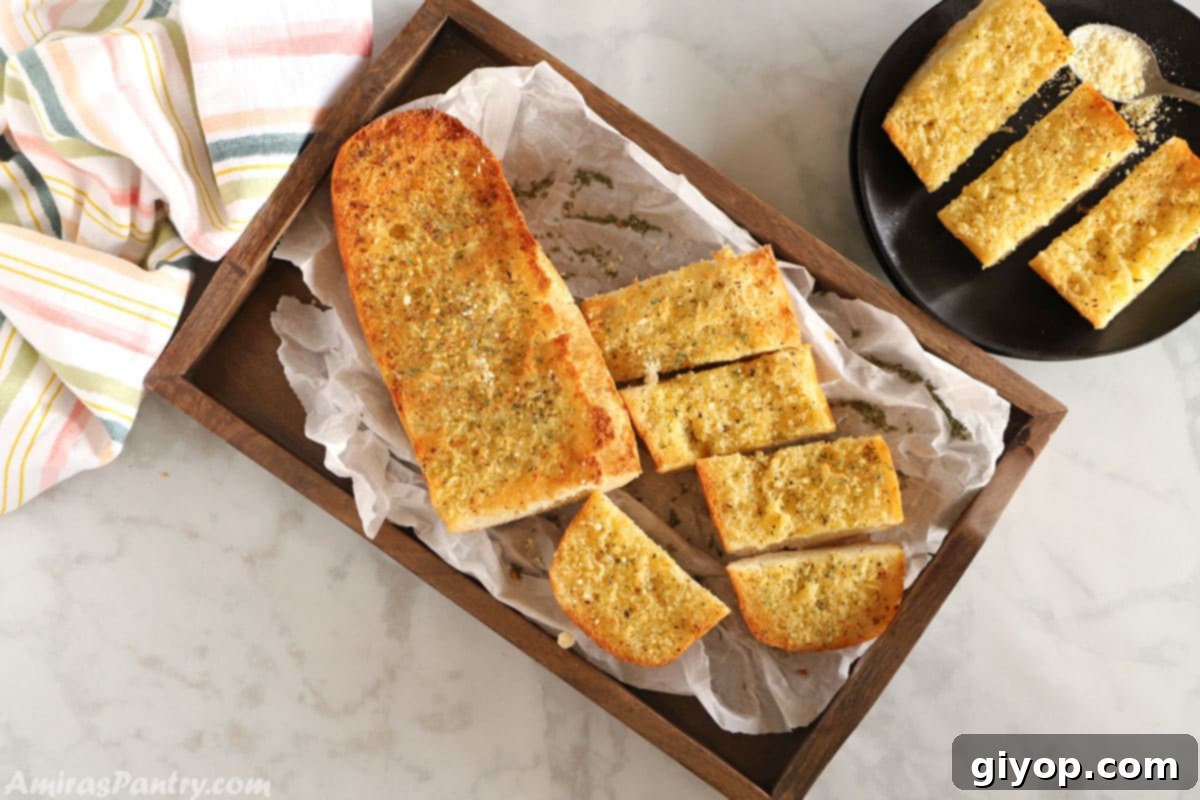 A top view image of garlic bread placed on a wooden tray with a plate of sliced garlic bread on the side.