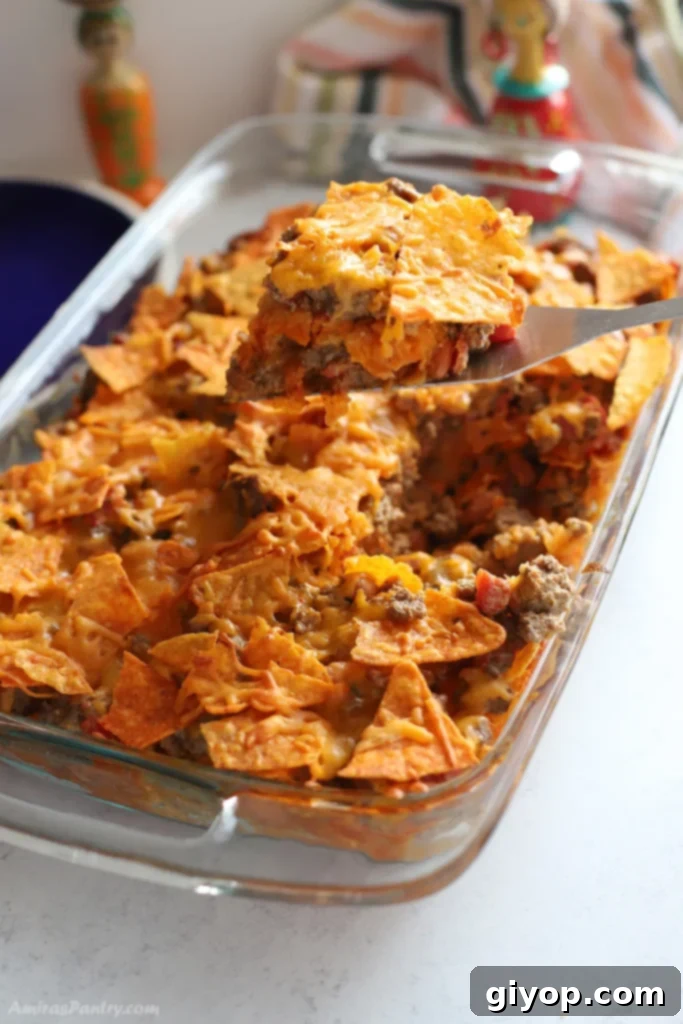 Meal Plan 8 6 A serving spoon lifting a generous, cheesy portion of the Ground Beef Doritos Casserole from a baking dish, highlighting its crunchy Doritos layer and savory beef filling.