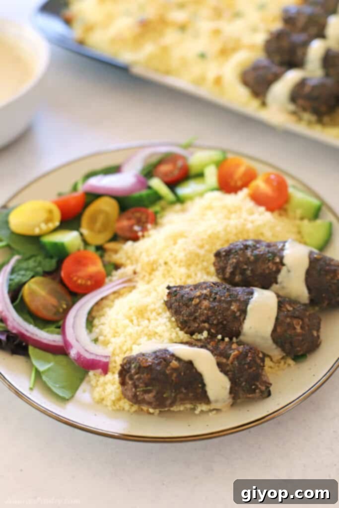 Kafta in a white plate drizzled with tahini sauce with green salad and couscous on the side.