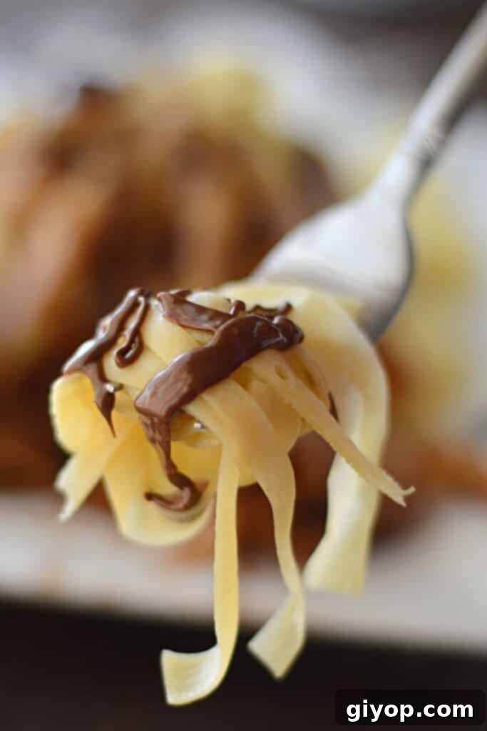 A fork with some fettuccine crepe drizzled with chocolate sauce, highlighting the delicate texture of the crepe.