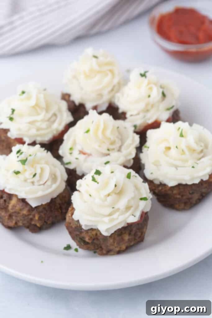Delightful meatloaf cupcakes individually served on a white plate, topped with creamy mashed potatoes.