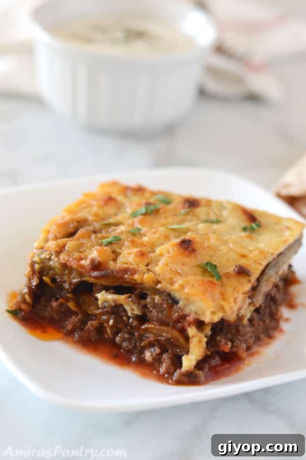 A moussaka piece on a white square dish on a marble white table.