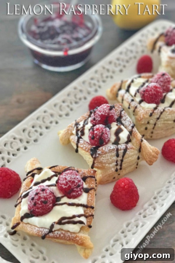 A hand elegantly holding a piece of golden-brown Lemon Raspberry Puff Tart, showcasing its flaky pastry and vibrant filling.