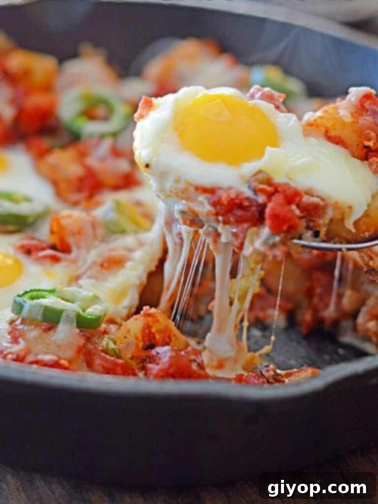 A spoon scooping an egg from a rustic cast-iron skillet of potato shakshuka, topped with melted cheese and fresh herbs.