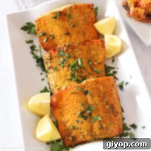 Air fried salmon pieces on a white platter garnished with lemon wedges and parsley.