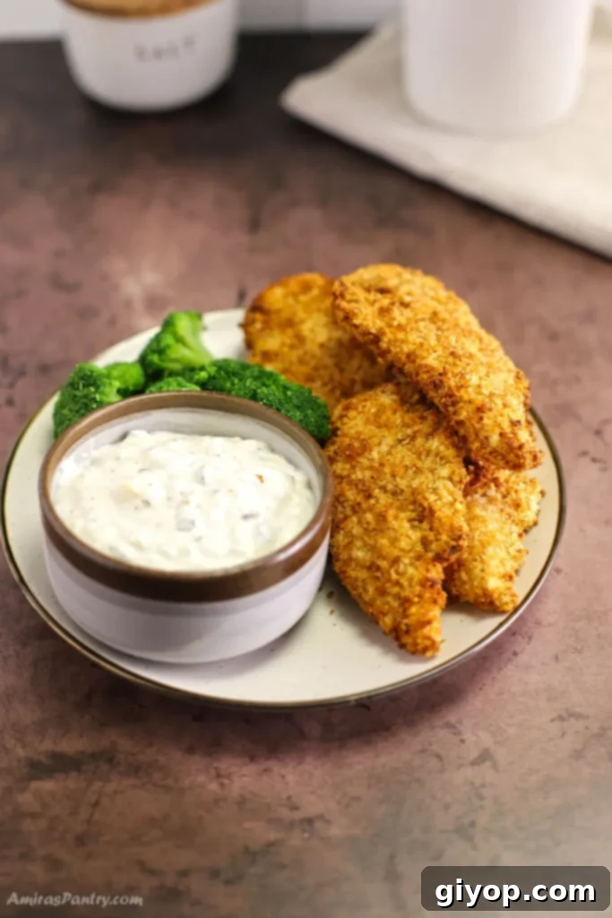 Perfectly golden brown Air Fried Chicken Tenders, incredibly crispy on the outside and juicy inside, served on a plate with a side of savory dipping sauce.