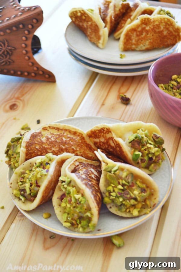 A plate of Qatayef Asafiri stuffed with cream and garnished with nuts, alongside a small bowl of pistachios.