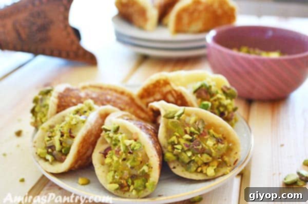 A white plate featuring a close-up of Qatayef Asafiri stuffed with cream, with other plates of Qatayef slightly blurred in the background.