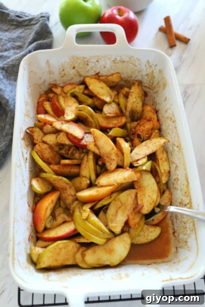 Your 28-Day Eating Guide 7 A white ceramic oven dish with healthy baked apple slices with a spoon in it, sprinkled with cinnamon.