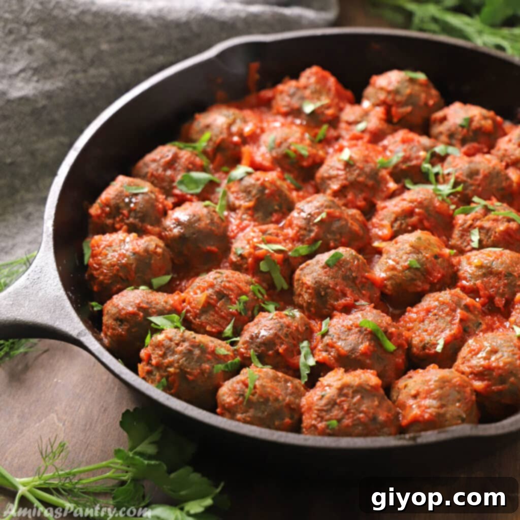Meatballs in a cast iron skillet with tomato sauce and garnished with parsley.