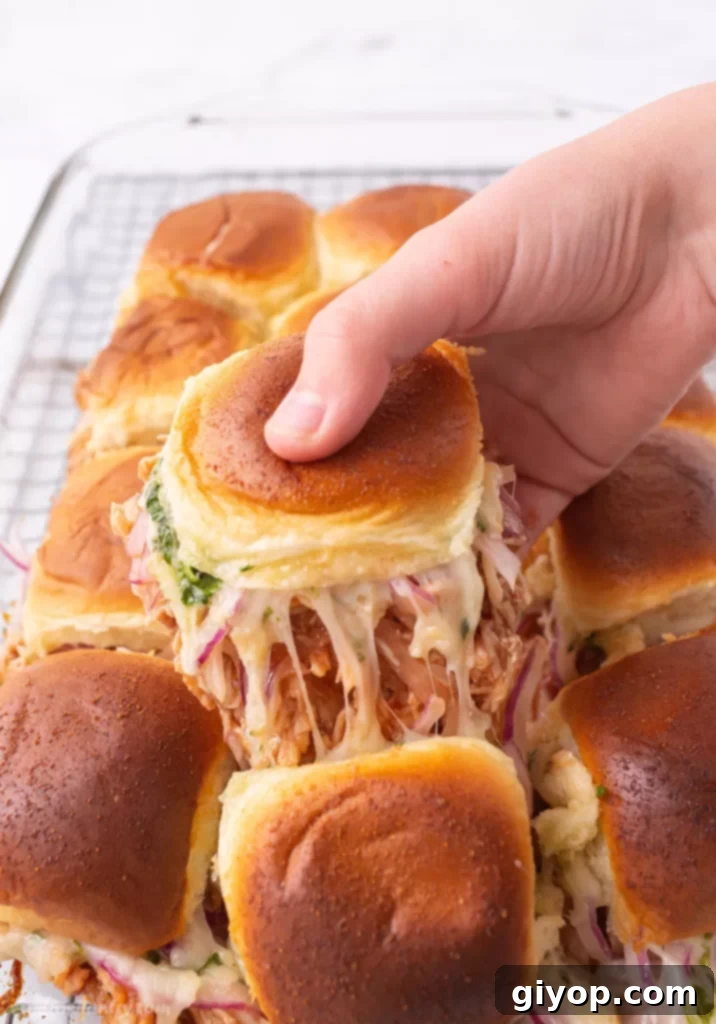 A hand pulling out a slider sandwich from a tray.
