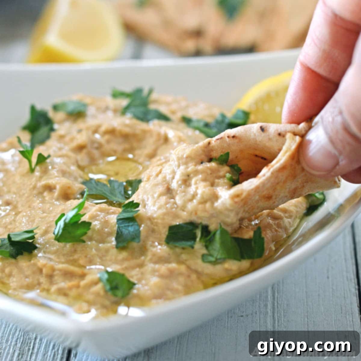 A hand scooping a generous portion of Baba Ganoush with a piece of warm pita bread, showcasing its creamy texture.