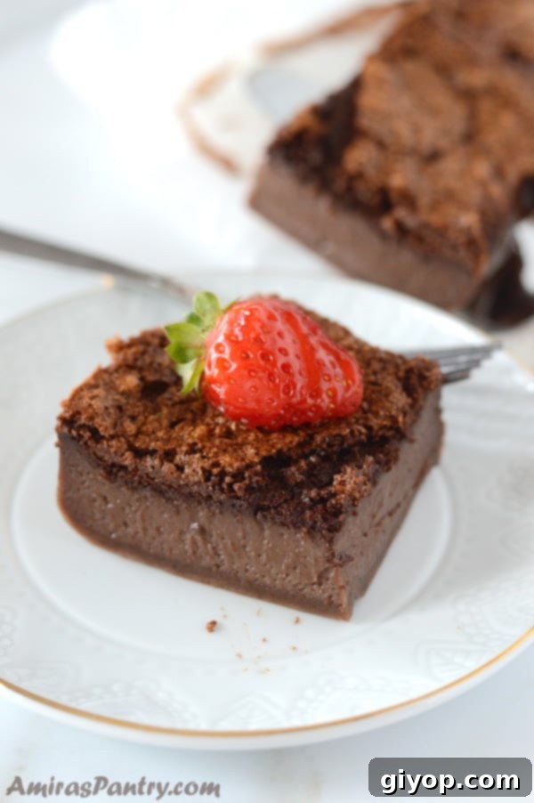 A slice of rich chocolate 'Magic Cake' on a white plate, elegantly garnished with a fresh strawberry.